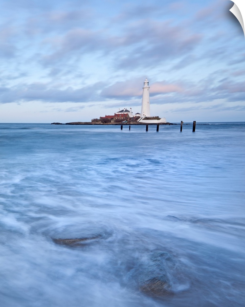 A dramatic image of swirling waves beneath a white Lighthouse and a blue sky at St. Mary's Bay, Newcastle, UK.