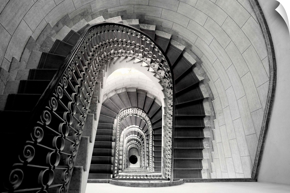This architectural photograph looks down a historic stairwell lined with tile and iron work banister.