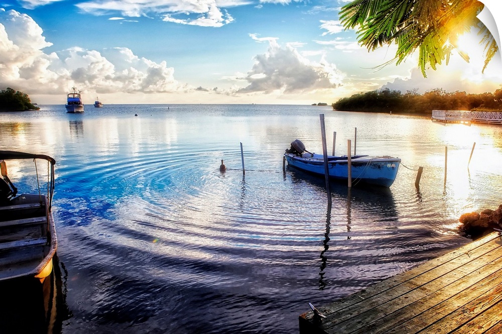 Huge photograph includes a number of boats sitting within a bay of a tropical island as the sun begins to set.  One of the...