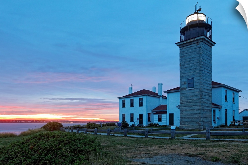 Photograph of lighthouse and building near water's edge under a cloudy sky at dusk.
