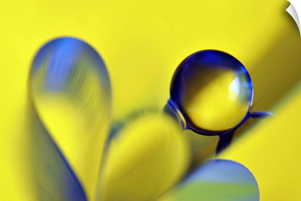 Macro abstract photograph of a water droplet reflecting on a yellow surface with blue ribbon-like designs below.