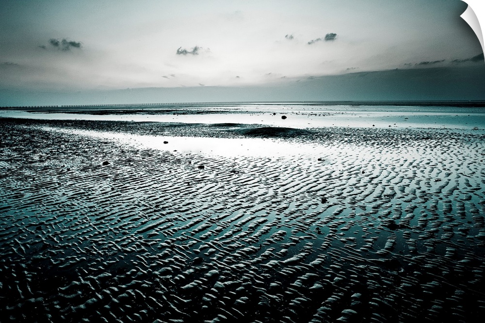 Big, landscape, fine art photograph of a wet, empty beach, surrounded by darkness beneath a gray sky.