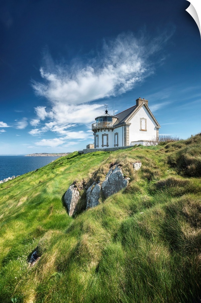 A photograph of a cozy cottage sitting on a hilltop overlooking an ocean.