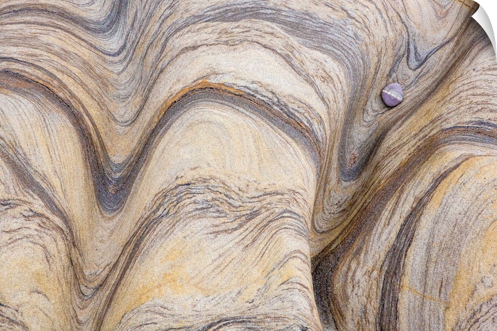 A contemporary image of flowing patterns in rock in neutral earth tones with a small lone pebble.