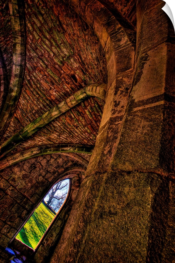 A dynamically angled gothic arched window beneath an ancient stone ceiling with views out to green fields and a winter tree.