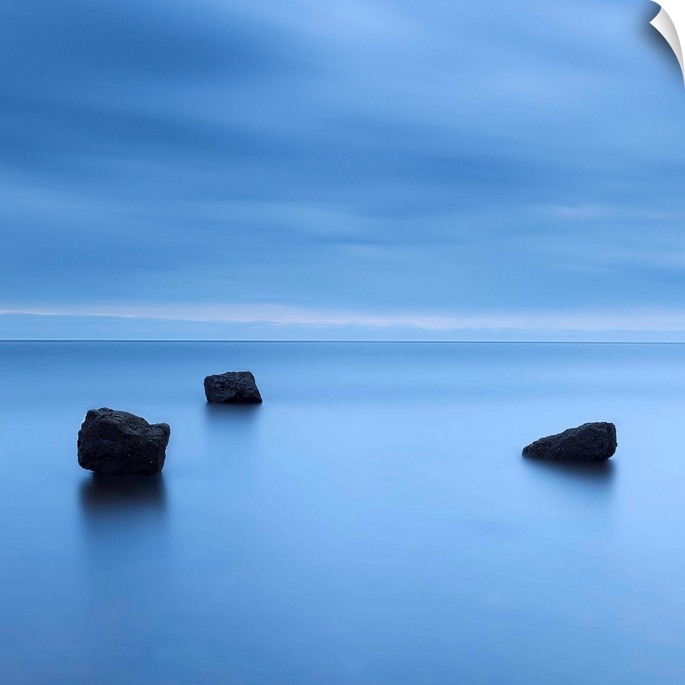 A zen calm minimal minimalist cool deep blue image of three rocks in a flat calm sea.