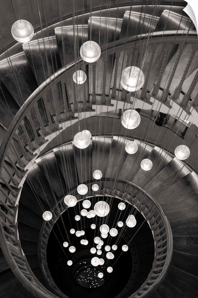 Fine art photo looking down a spiral staircase, with round lights in the center, in black and white.