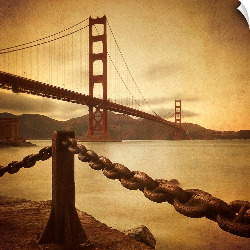 This large square print is a low angle view of the Golden Gate Bridge from land where there is a large chain shown in fron...