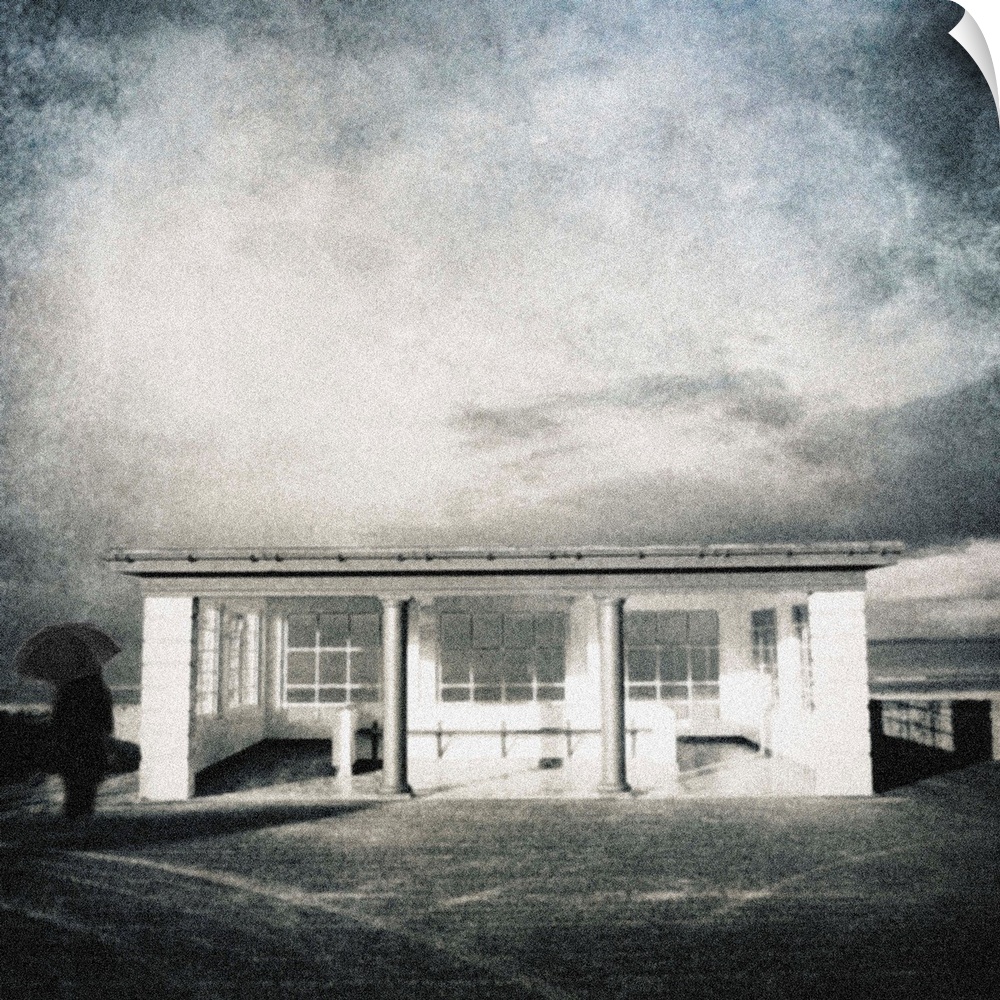 A surrealist vintage image of a small English seaside seafront shelter in white with a man holding a black umbrella.