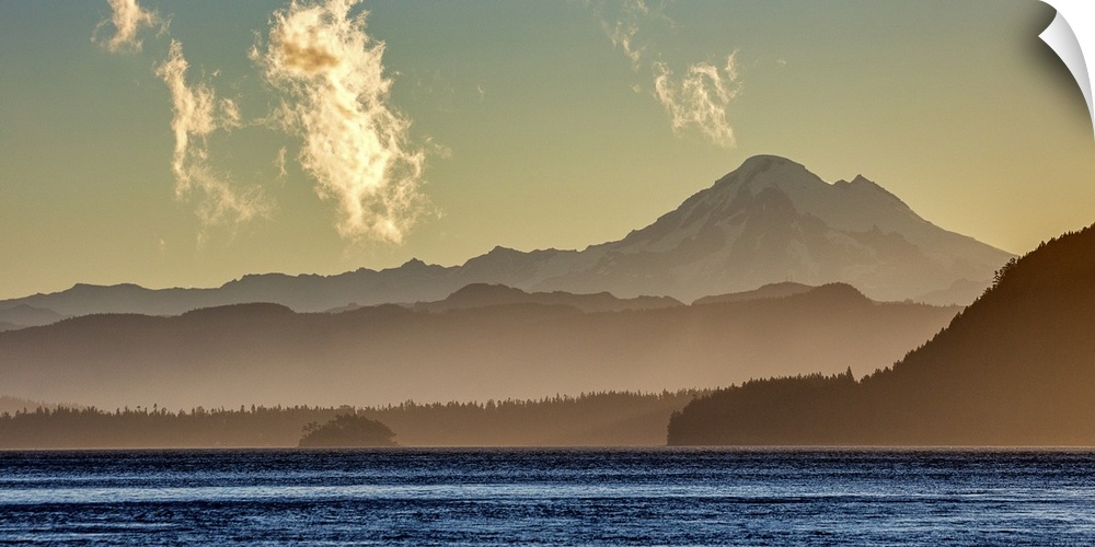 Mist surrounding the mountains on the Washington coast in dim sunlight with the bright blue ocean in the foreground.