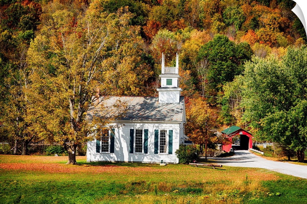 A Baptist church in a forest with fall foliage and a covered bridge visible in the distance.