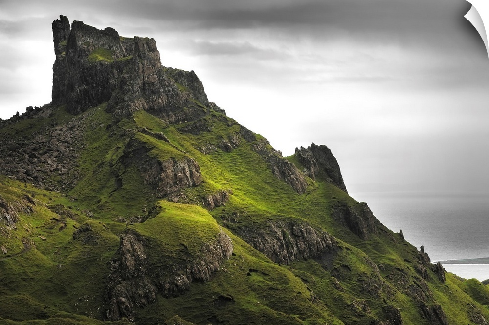 Fine art photo of rocky spires on a green hill under a cloudy sky.
