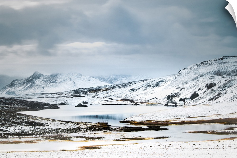 Scottish Mountains in the snow with a small cottage beside a lake.