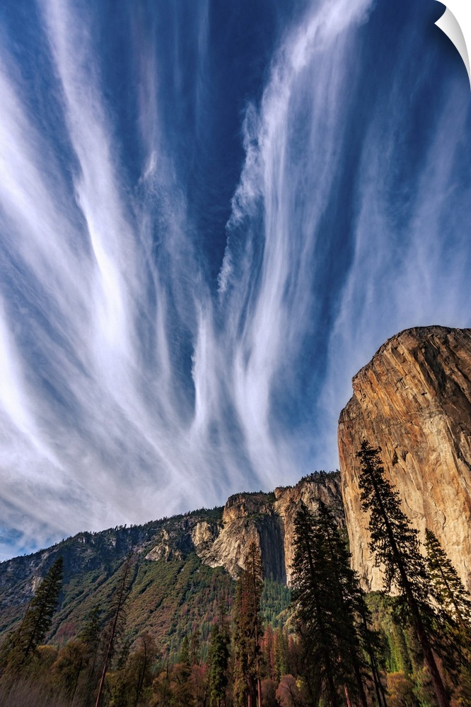 This picture features clouds dramatically streaking the blue sky fanning out above Yosemite's El Capitan cliff.