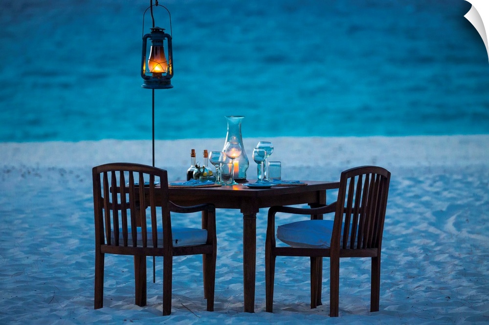 A photograph of a romantic table setting on a sandy beach at sunset.
