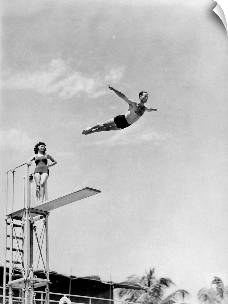 1930s 1940s Shapely Woman Watching Man Swan Dive Off High Diving Board.