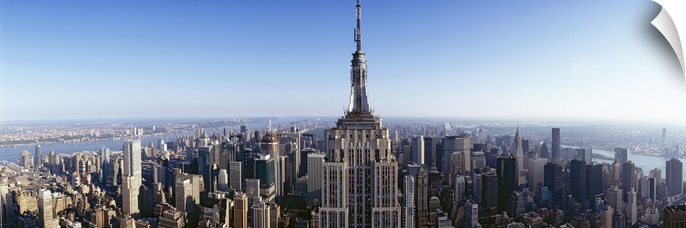 Wide angle, aerial photograph of New York City beneath a blue sky, the Empire State Building in the foreground.