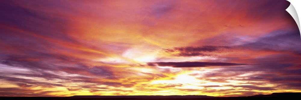 A panoramic photograph of clouds lit up in brilliant colors from the sun below the horizon.