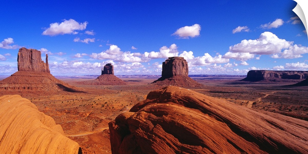 Large panoramic photograph taken of Monument Valley with giant rock formations seen in the distance under a beautiful blue...