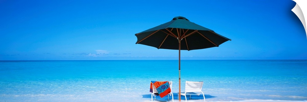Two beach chairs under an umbrella in front of the ocean in the sand on the Turks and Caicos Islands.