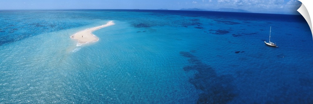 Panoramic, aerial photograph of clear blue waters over the Great Barrier Reef, a single sailboat in the water, in Queensla...