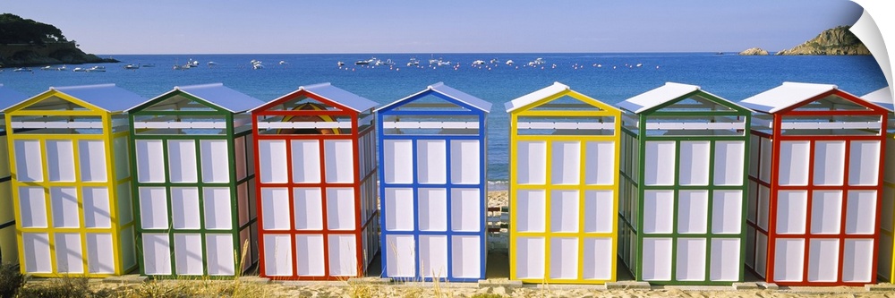 Panoramic photograph of colorful row of huts on the shoreline with the ocean in the distance.