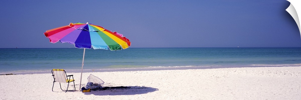 Panoramic photograph of beach chair and parasol in the sand, with ocean fading into the distance.  The sky is clear.