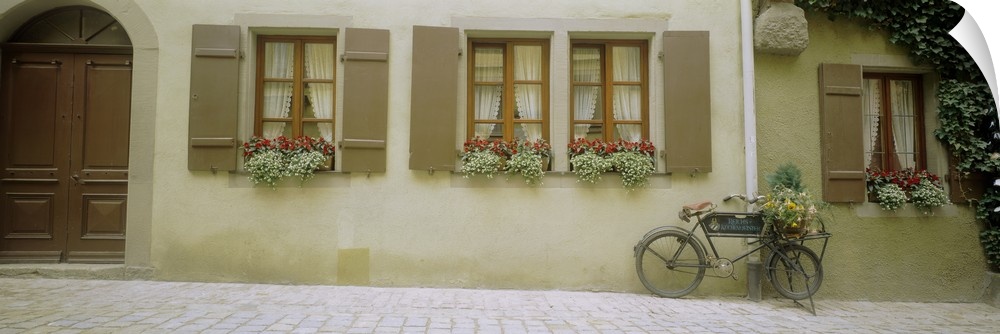 Panoramic photograph of home with huge wooden arched door, windows, shutters, and flowerboxes.