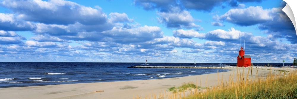 Panoramic photograph of a large lighthouse next to a dock on a sandy beach in Holland, Michigan during a sunny day.  The w...