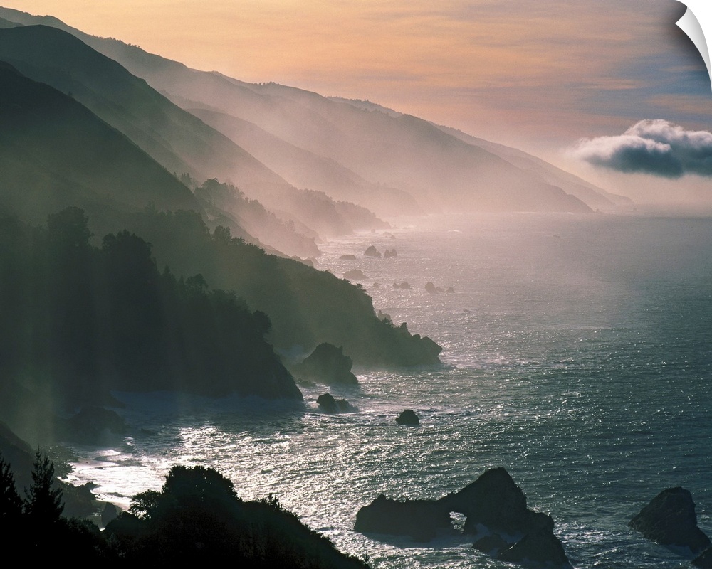 Photograph of the Santa Lucia Mountains rising through fog and mist from the Pacific Ocean.  The sky is warm with clouds i...