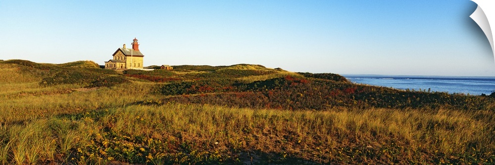 A large lighthouse is photographed in panoramic view surrounded by open grassy land.