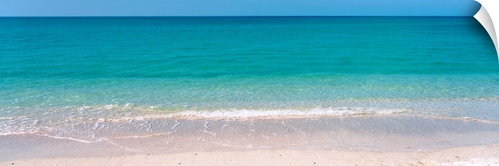 A panoramic photograph of a calm sea of tropical colored water.
