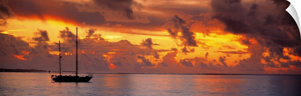 Single ship with two tall masts on calm waters against a backdrop of dramatic fiery clouds at dusk.