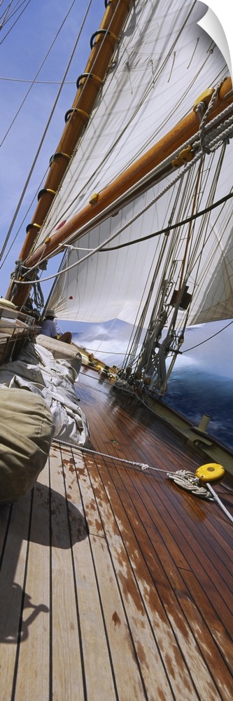 Vertical panorama of the deck of a sail boat as it tips starboard in water with the sails at full mast.
