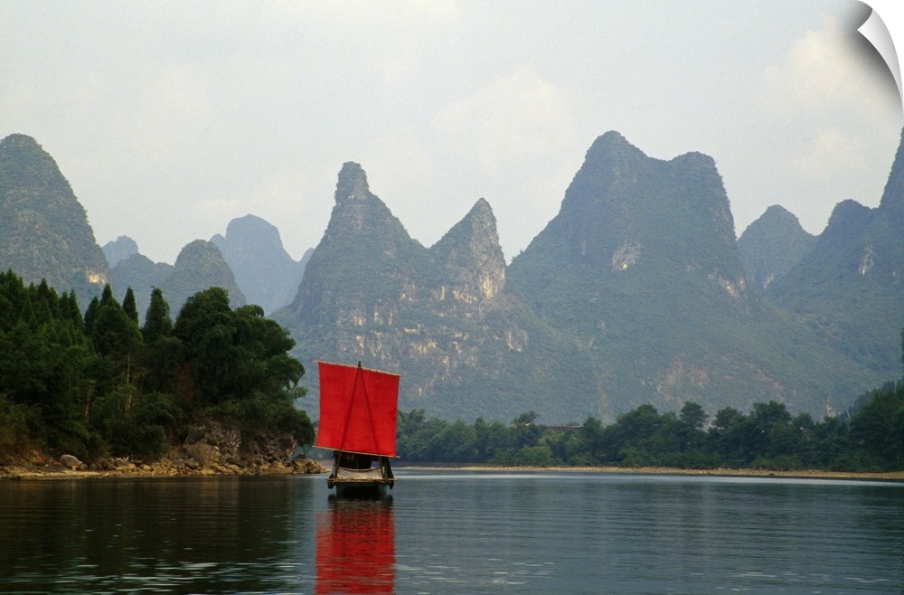 A small boat in a Chinese river is photographed in front of immense cliffs.