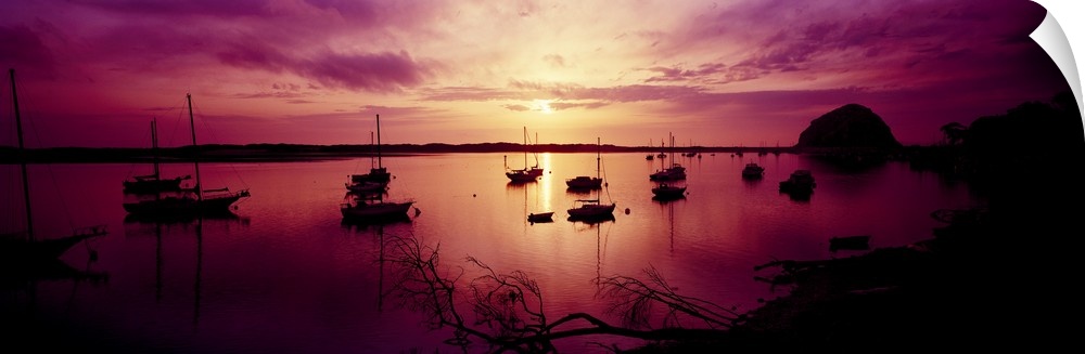 Several boats sit in a bay off of the California coast as the sun starts to set off in the distance and casts a purple sha...