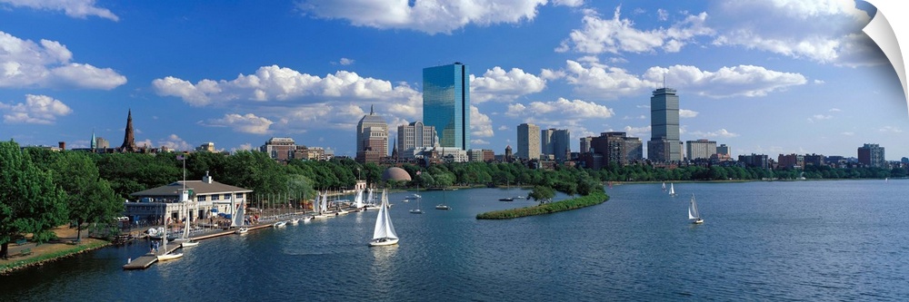 Panoramic photograph of skyline and waterfront under a cloudy sky, with sailboats in the water.