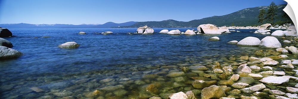 Panoramic view of Lake Tahoe with a line of rocks on the bottom and toward the right side of the picture. Mountains are sh...