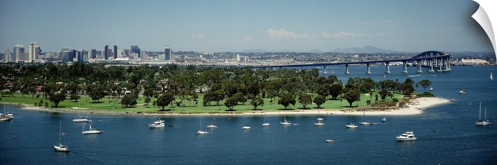 Panoramic photograph of many small boats and an area of land with many trees near the bay, next to the Coronado Bridge in ...
