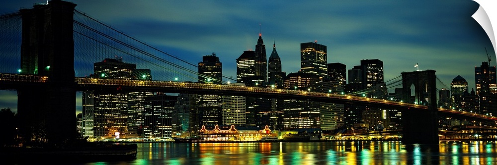 A panoramic photograph of Manhattan harbor lights reflecting in the East River at night.