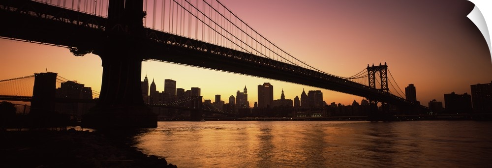 The Manhattan bridge and New York City skyline are silhouetted by the sunset.