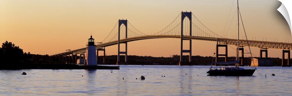 Panoramic photograph of overpass in New York with lighthouse and boat in front of it at sunset.