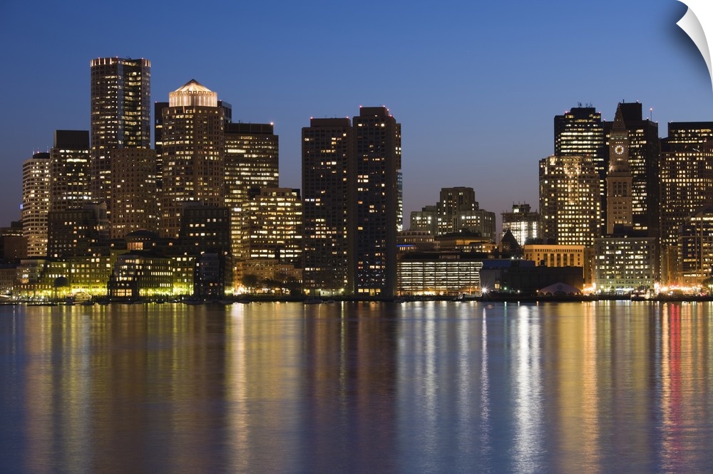 The evening city lights create a blurred reflection in the bay in New England, the darkened skyscrapers rising against a p...