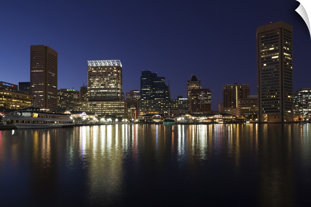 City skyscrapers reflecting their lights onto the water of the Inner Harbor in Baltimore, Maryland.