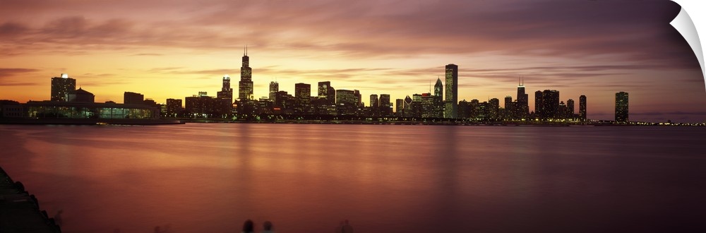 Wide angle, distant photograph of lit skyscrapers of Chicago, over the waters of Lake Michigan, at sunset.