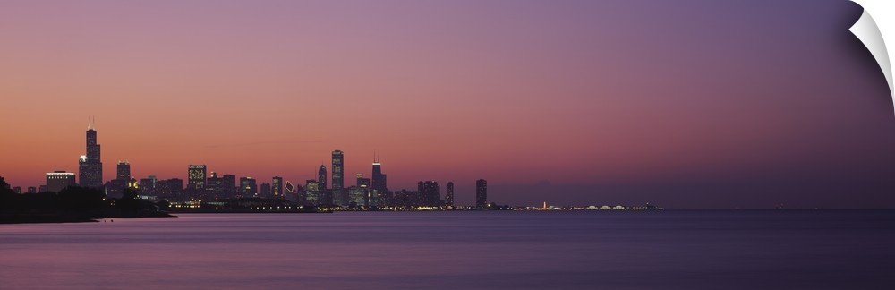 The Chicago skyline is skewed to the left of this panoramic piece and silhouetted by a sunset sky. Lake Michigan largely t...