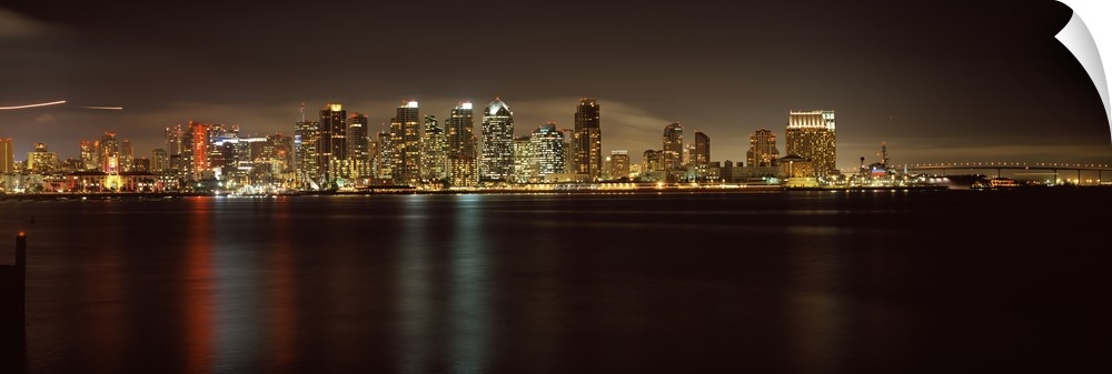 Panoramic photograph of the San Diego city skyline along the edge of the bay in the evening, the waters reflecting the cit...
