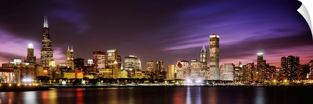 A big cityscape panoramic of downtown Chicagoos lights reflecting off Lake Michigan at night.