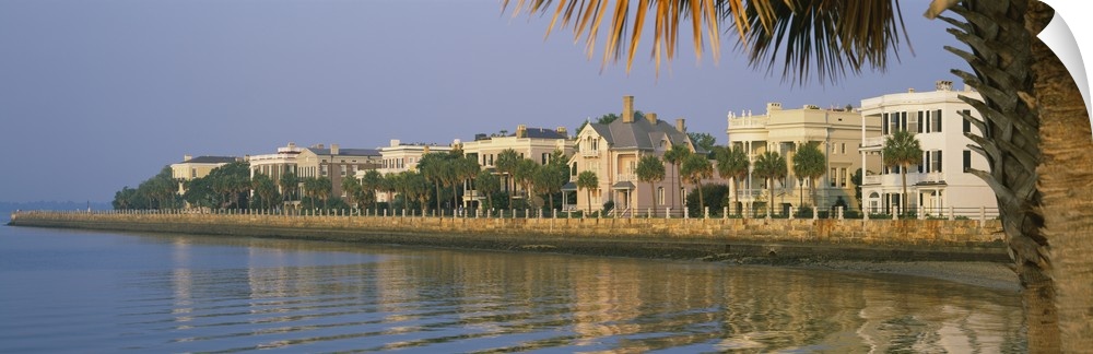A panoramic picture taken of houses on the waterfront in Charleston. Palm trees line the right side of the picture with so...