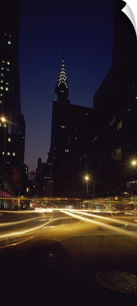 Vertical panoramic photograph of street with light trails lined with lit up buildings in the ""Big Apple.""